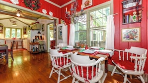 Un comedor con una decoración en tonos rojo y blanco, suelo de madera y sillas blancas con cojines rojos.
