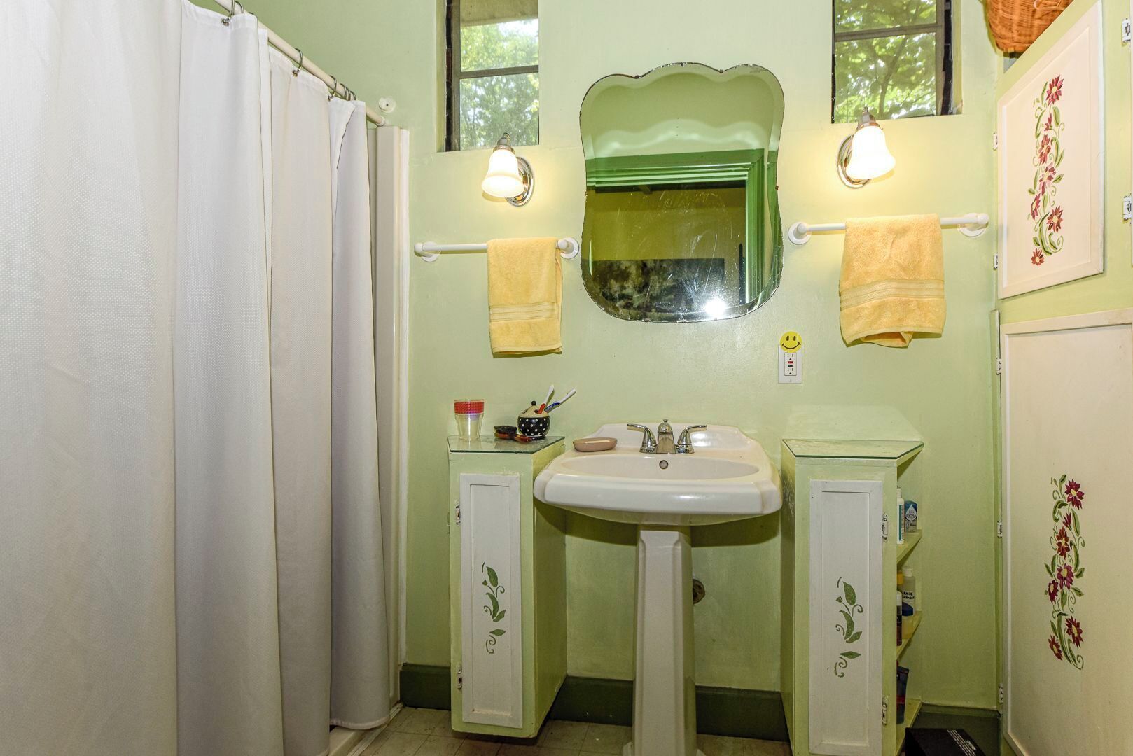 A bathroom with a shower curtain, two sinks, a mirror, and a window.