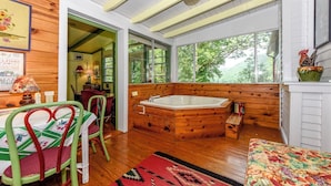 Interior de una cabaña con detalles de madera, un jacuzzi y amplios ventanales con vistas al exterior.