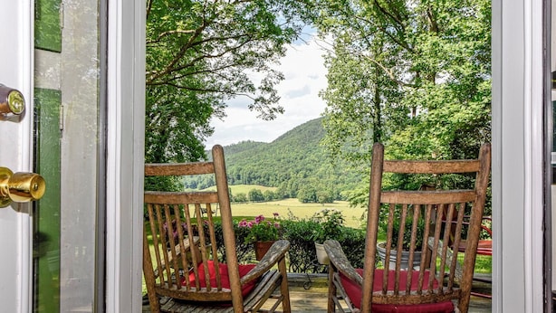 Una puerta de madera con dos mecedoras mirando hacia un paisaje verde exuberante.