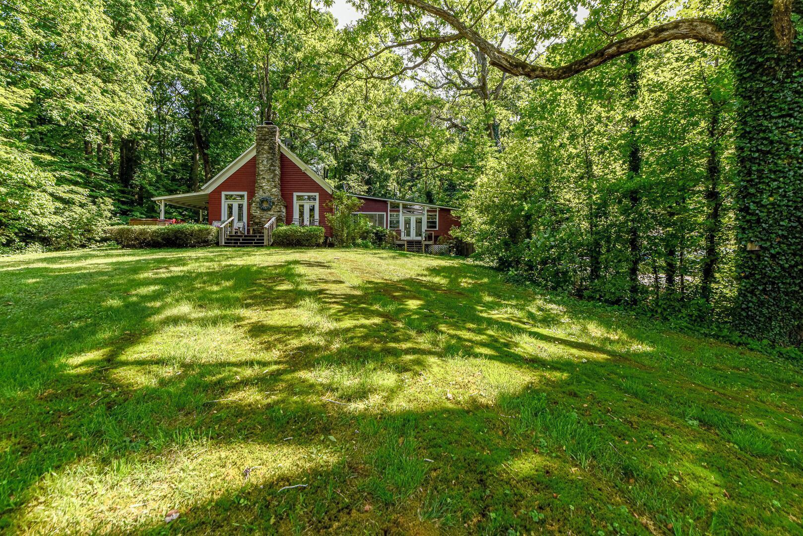 A red house with a stone chimney, surrounded by lush greenery and trees.