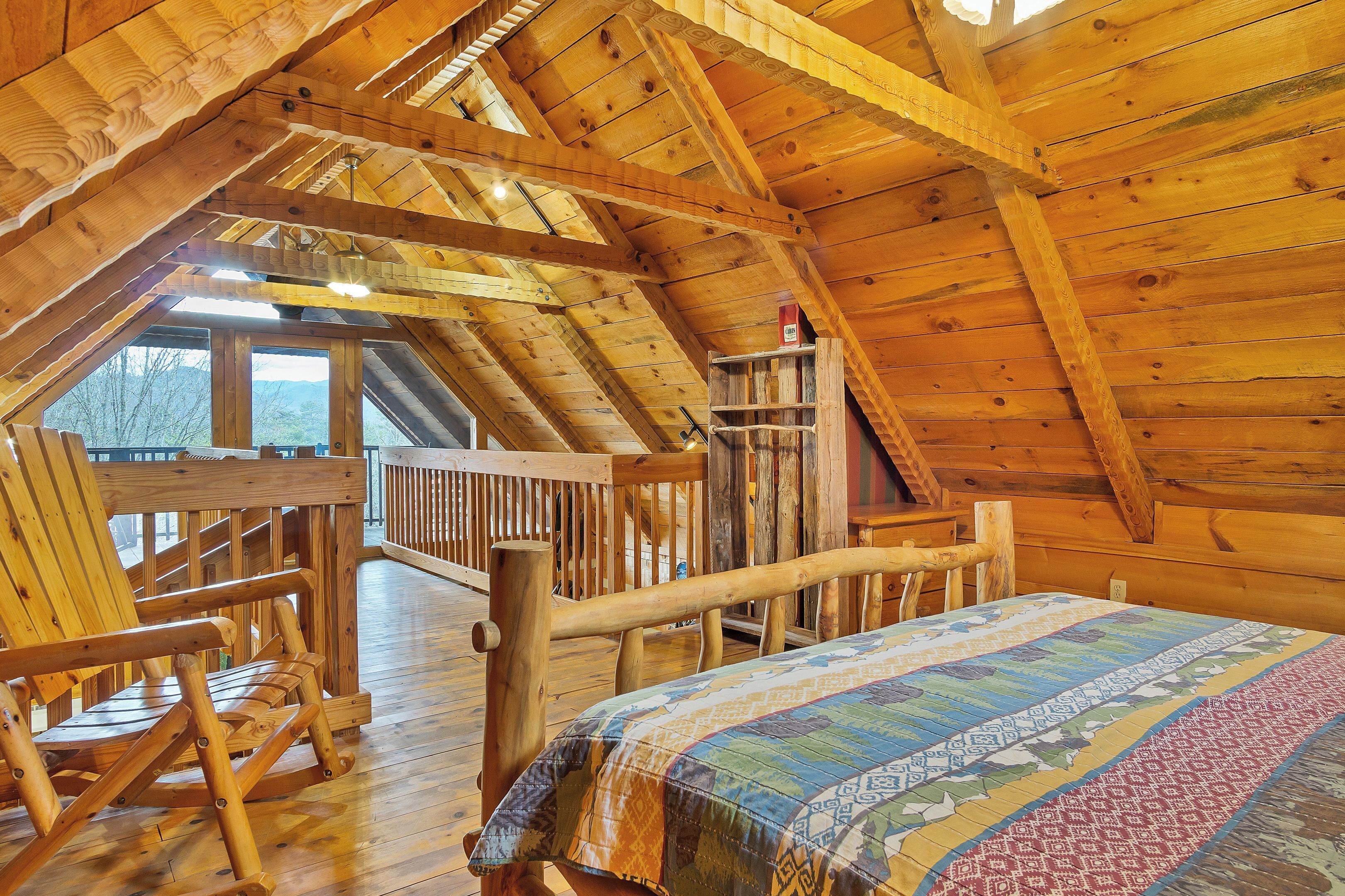 A wooden interior with a high ceiling, a bed with a patterned bedspread, wooden chairs, and a wooden railing.