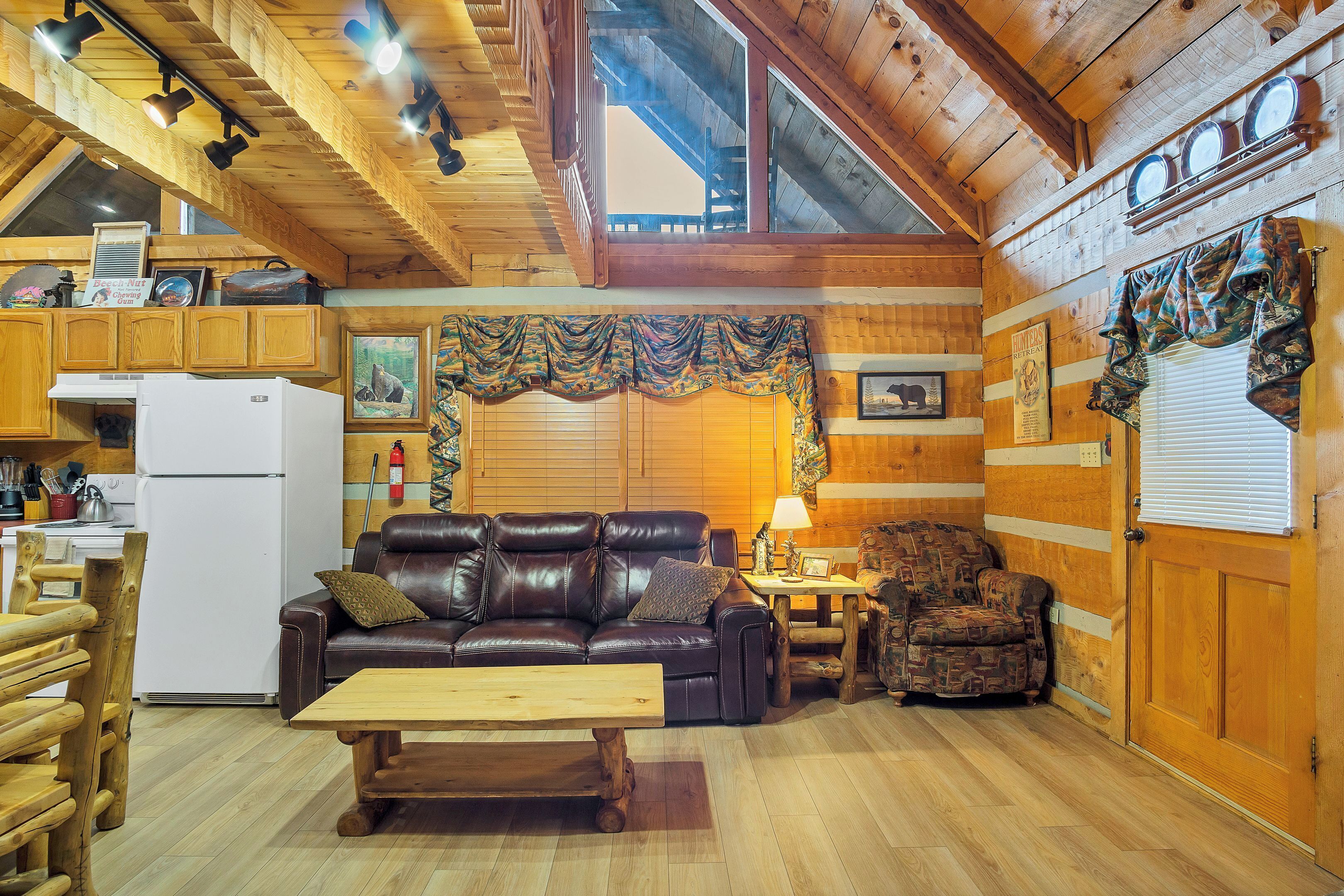 A cozy cabin interior with a wooden ceiling, a dining area, a sofa, and a patterned armchair.