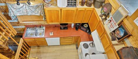 A compact kitchen with wooden cabinets, a sink, a stove, and a dining area with a table and chairs.