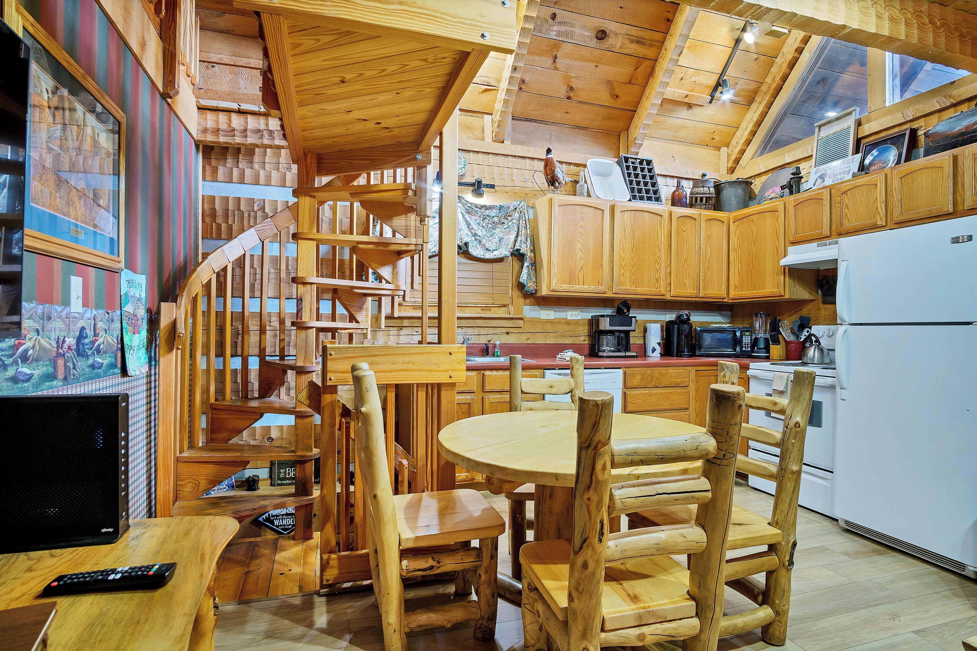 Un intérieur en bois comprenant une table à manger, des chaises, un coin cuisine avec un réfrigérateur et un escalier.