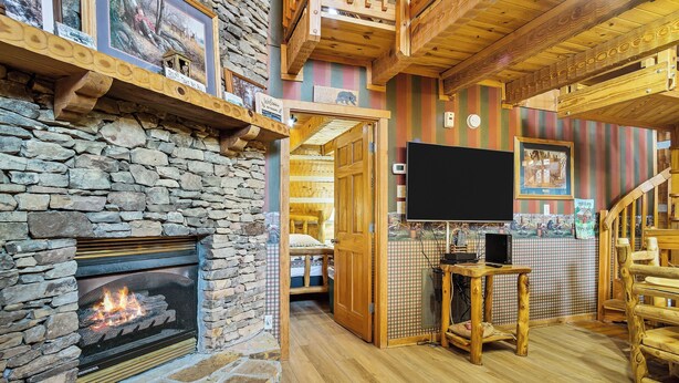 Um quarto acolhedor com lareira de pedra, vigas de madeira, televisão e escada.