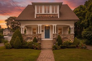 A two-story house with a front porch, stone foundation, and a blue door.