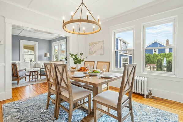 A dining area with a wooden table set for four, surrounded by chairs, a chandelier, and a view of the outside.