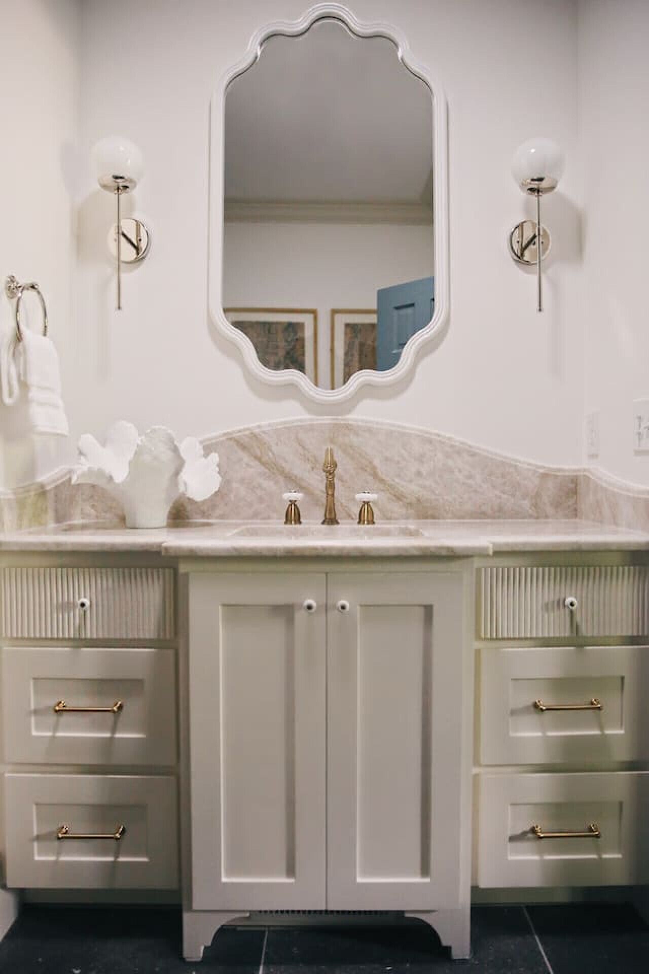 A bathroom with a marble countertop, a large mirror, and two wall-mounted light fixtures.
