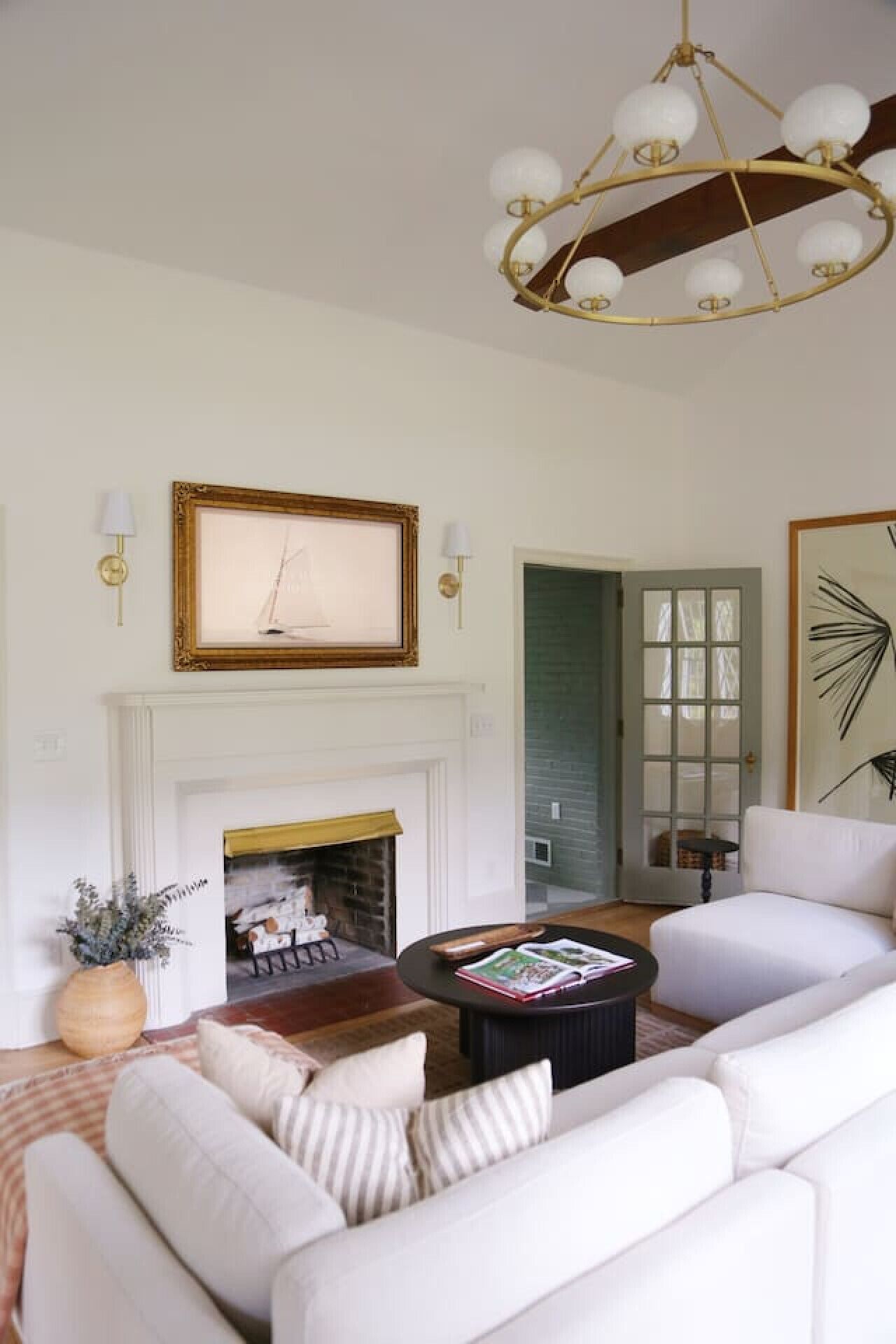 Un salon avec un canapé blanc, une cheminée, un lustre et un tableau encadré au-dessus de la cheminée.