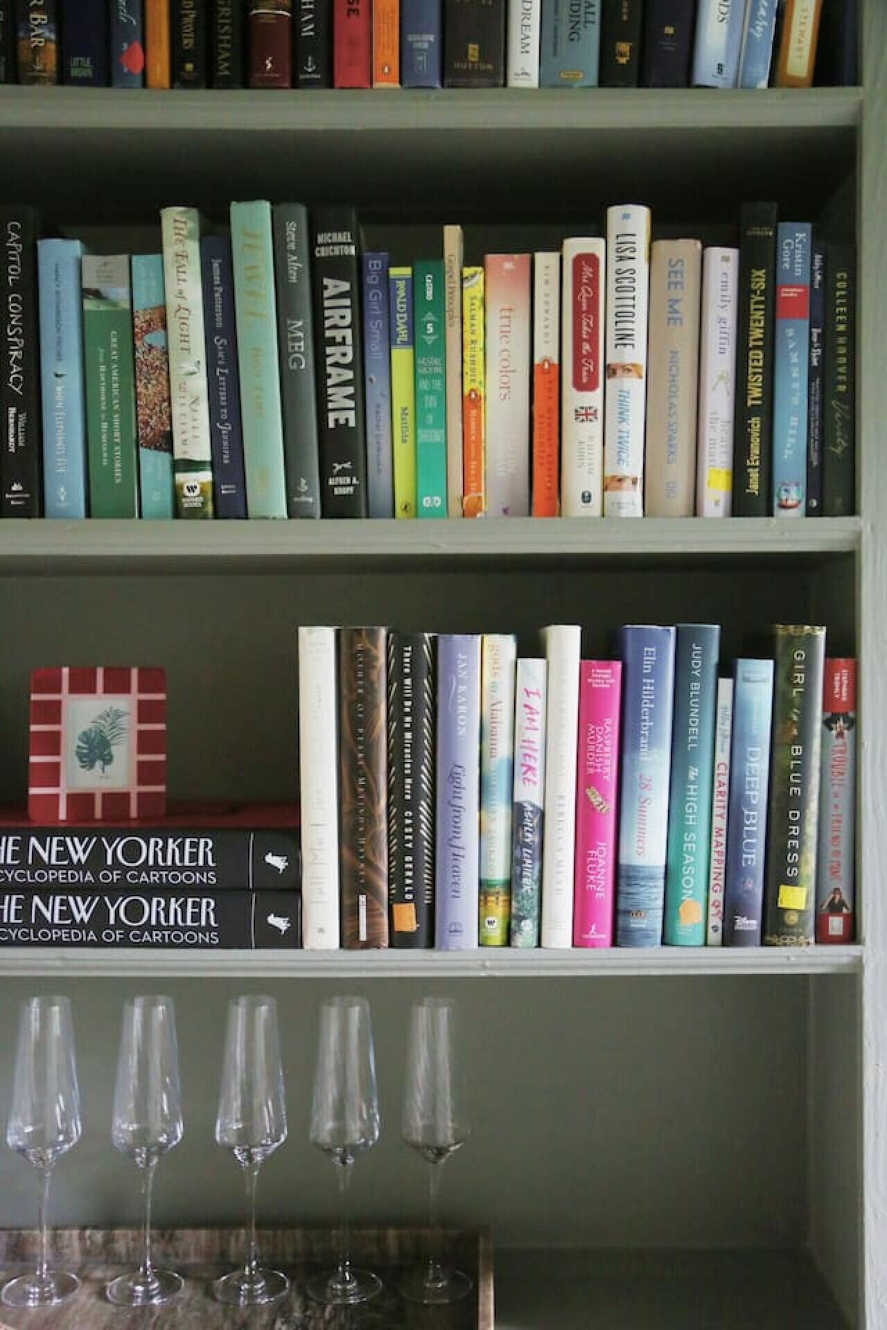 A bookshelf with a variety of books and a small display of wine glasses.