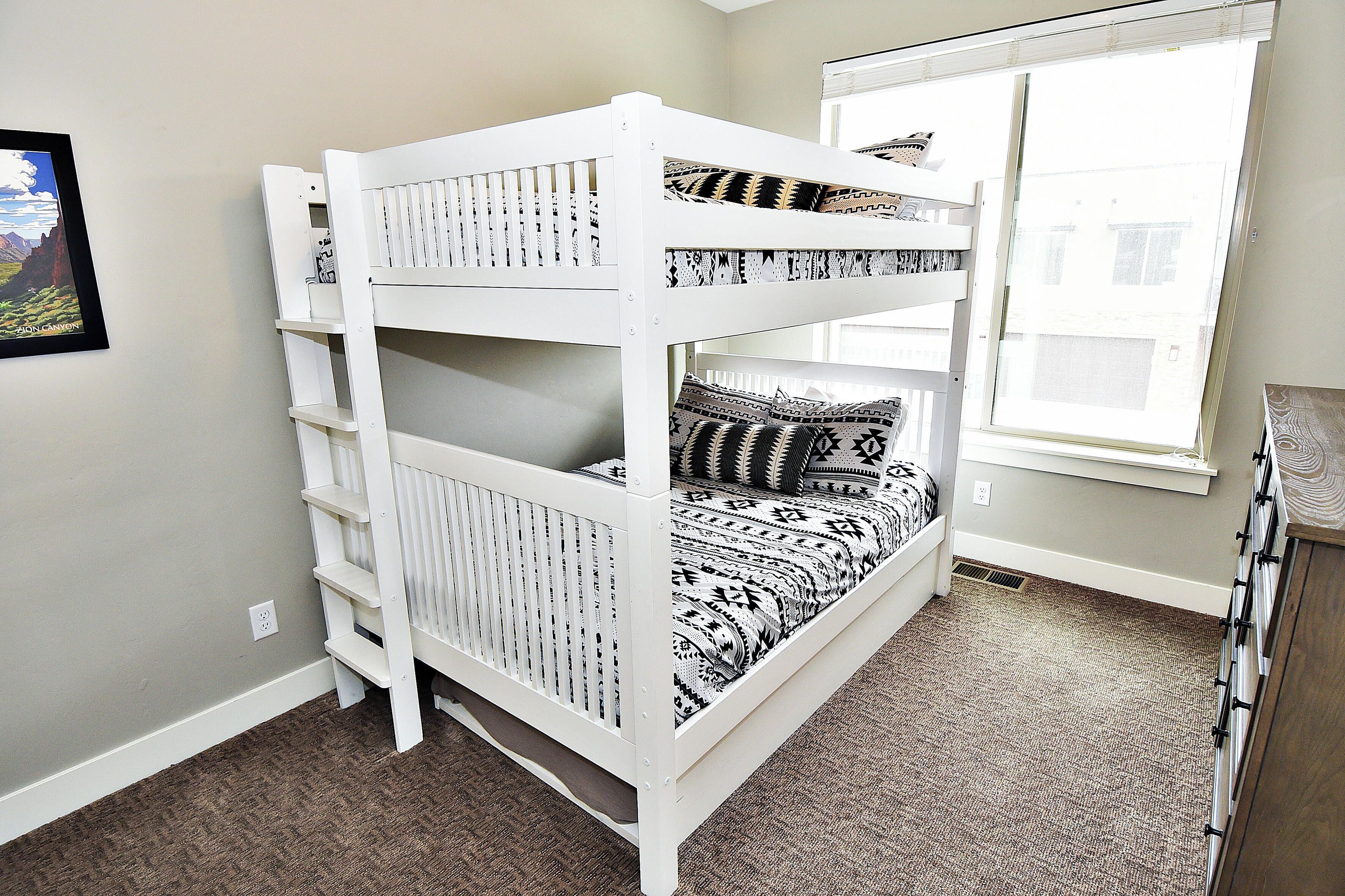 A bunk bed with patterned bedding, a window with blinds, and a carpeted floor.
