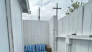 Eine schmale Terrasssengelände mit zwei Korbuschlaubsofas mit gestreiften Kissen, einer dekorativen Metall-Fußmatte und einer weißen Backsteinwand.