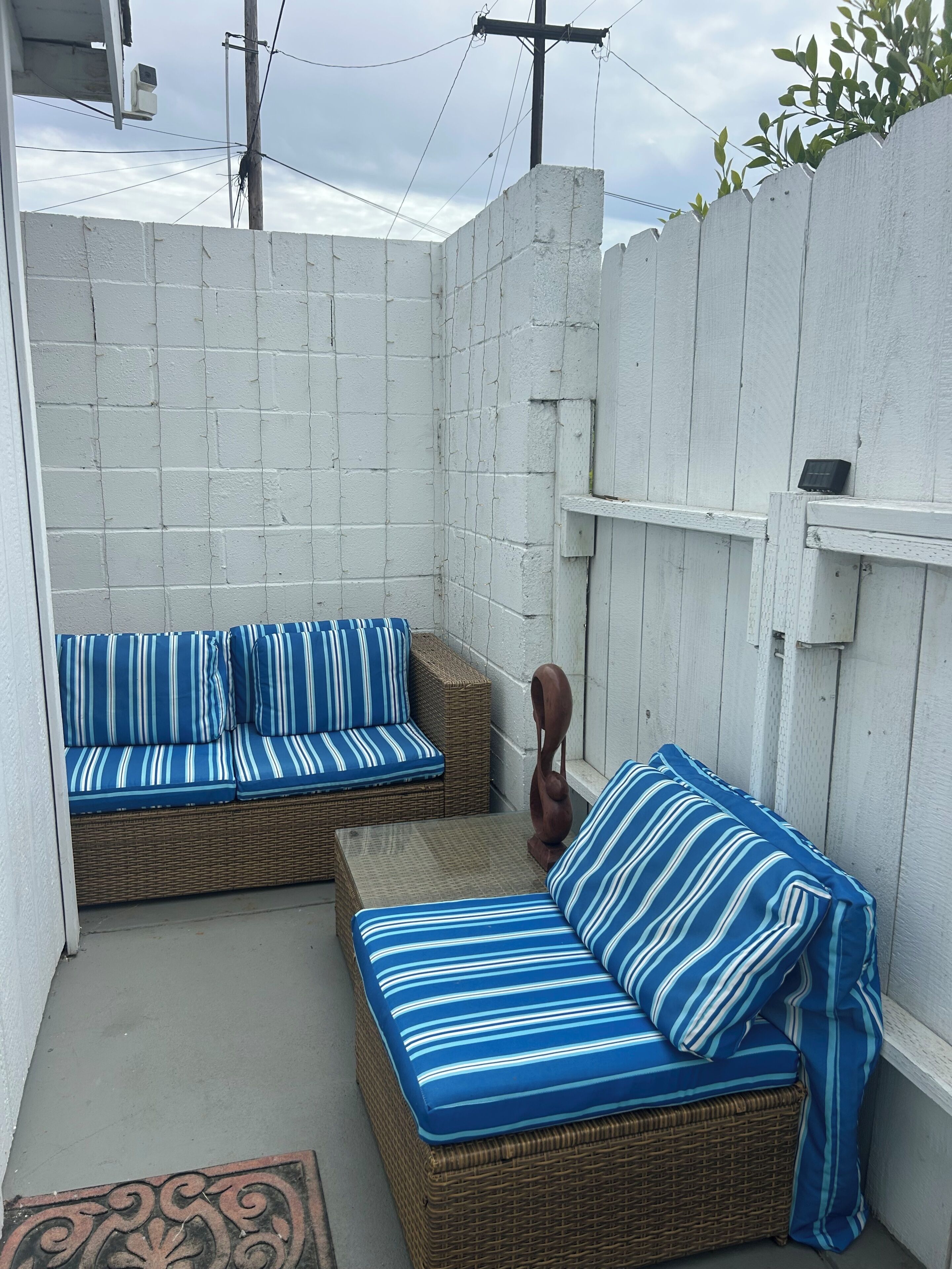 Un pequeño espacio al aire libre con dos sofás de mimbre y cojines, una mesita y una escultura de madera decorativa.