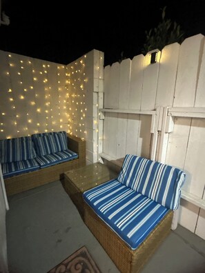 An outdoor seating area with two wicker sofas and a table, surrounded by a white fence and string lights. - Perfect guesthouse near Downtown San Diego (National City)