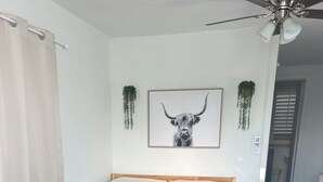 A bedroom with a bed, a ceiling fan, a framed picture, and a small side table.