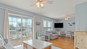 Un salón amplio con un gran ventanal, un sofá blanco, una mesa de centro y un televisor.