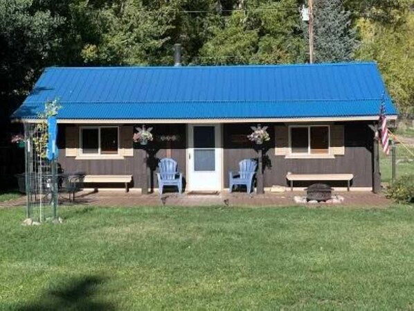 A single-story building with a blue roof, a front porch with two chairs, and an American flag.