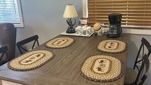 Ein Esstisch mit vier gewebten Platzsets, einer Kaffeemaschine und einer Lampe.