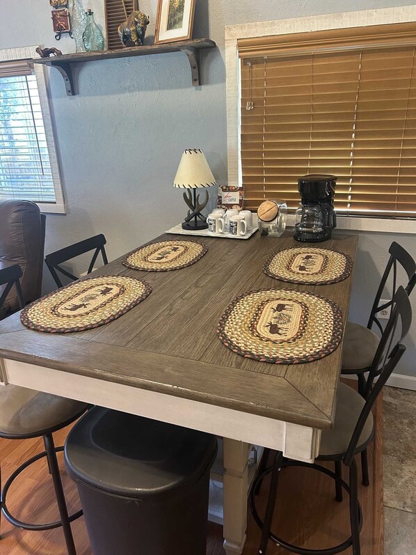 Una mesa de comedor con cuatro individuales tejidos, una cafetera y una lámpara.