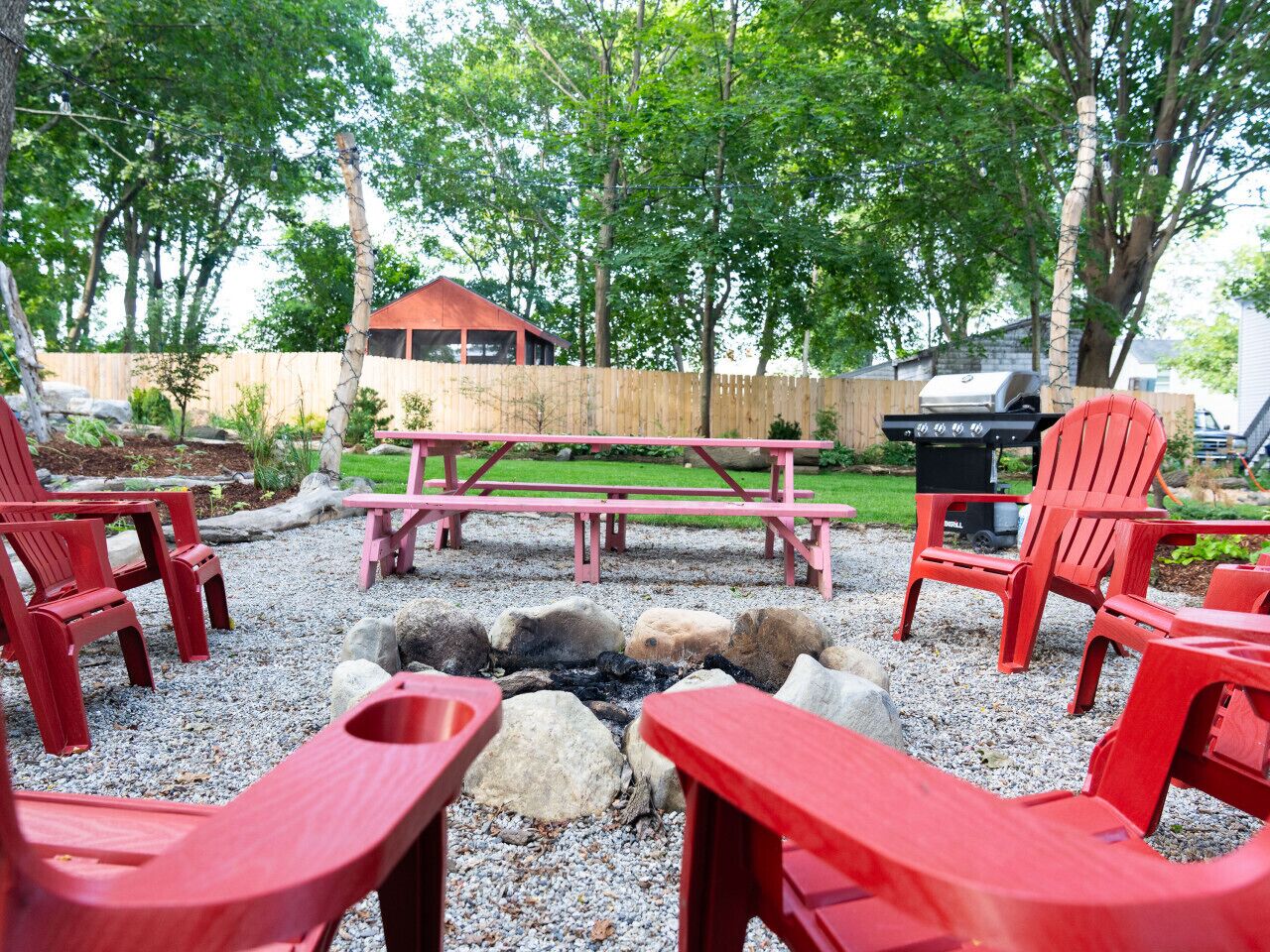 Un pati amb una xemeneia, seients Adirondack vermells, una taula de picnic i una barbacoa.