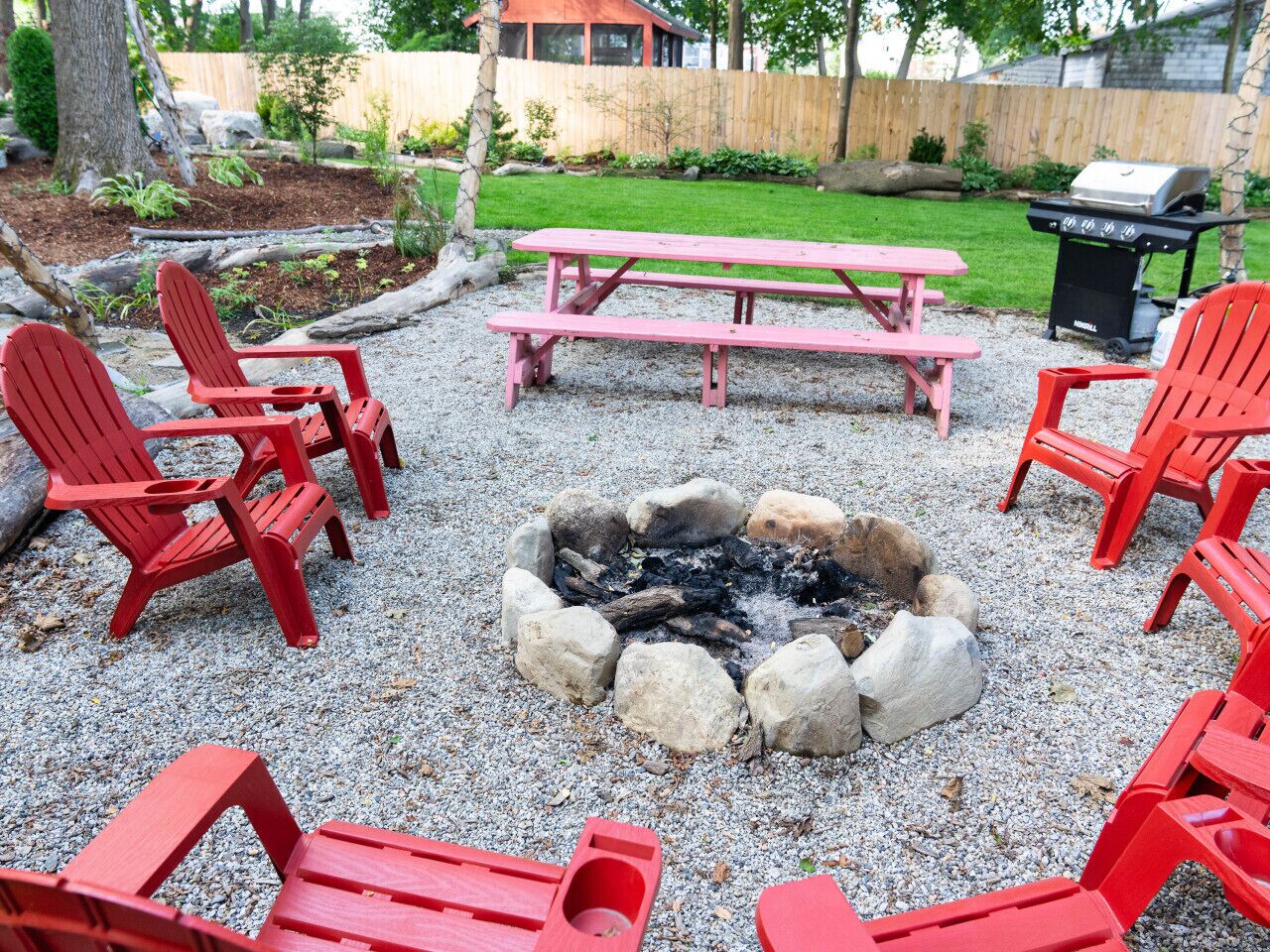Un jardin avec un foyer entouré de chaises Adirondack rouges et d’une table de pique-nique.