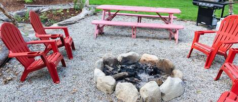 Un jardin avec un foyer entouré de chaises Adirondack rouges et d’une table de pique-nique.