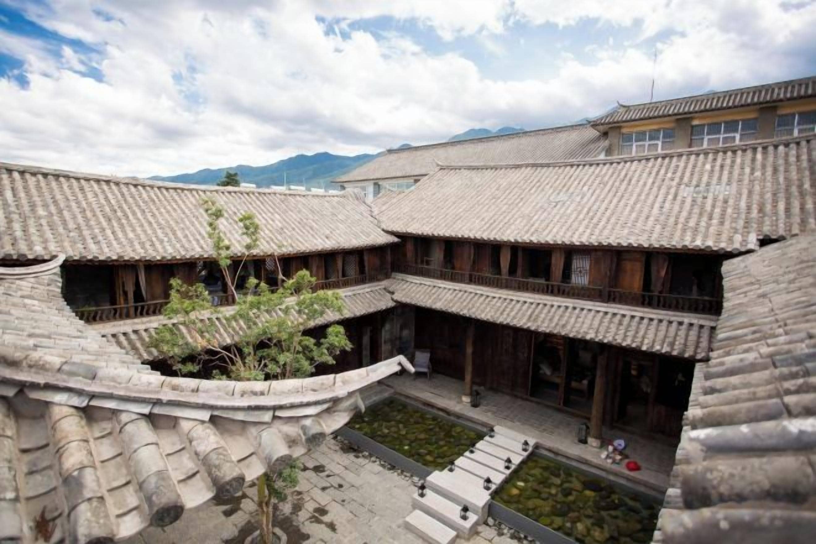 A traditional courtyard with tiled roofs and wooden structures, surrounded by mountains.