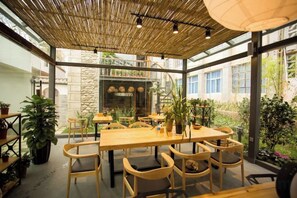 An indoor dining area with a wooden table and chairs, surrounded by potted plants and a glass wall. - Manyue Wangjiayuan Hostel (Dali City)