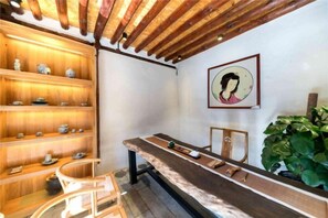 A room with a wooden ceiling, a long table, shelves with cups, and a framed picture on the wall. - Manyue Wangjiayuan Hostel (Dali City)