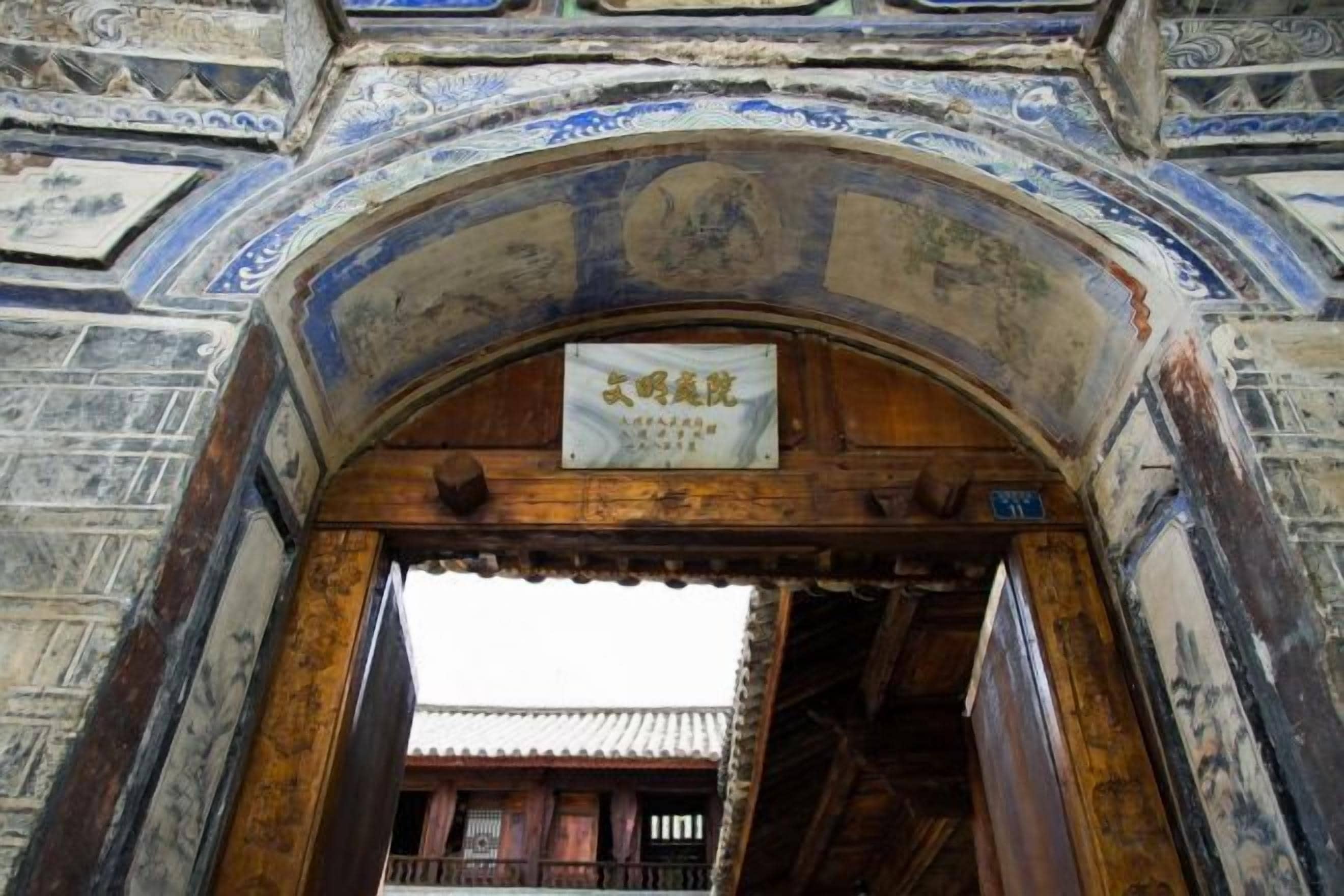 An arched entrance with a sign, wooden door, and traditional Chinese architectural elements.