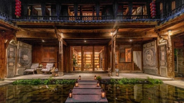 A traditional wooden building with a central courtyard, stone steps leading to a water feature, and a balcony with red lanterns. - Manyue Wangjiayuan Hostel (Dali City)