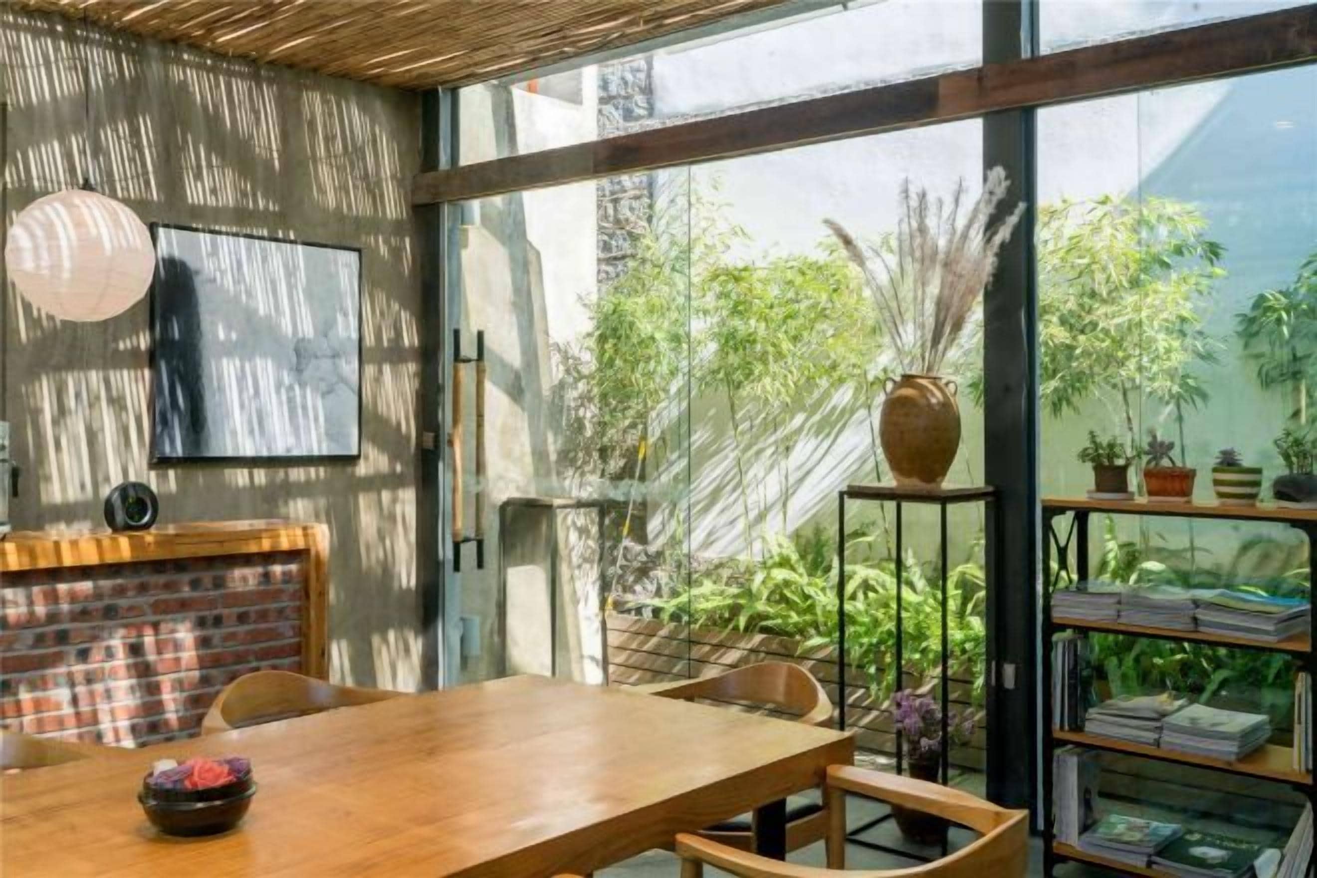 A dining area with a wooden table and chairs, a brick wall, and a large window overlooking a garden.