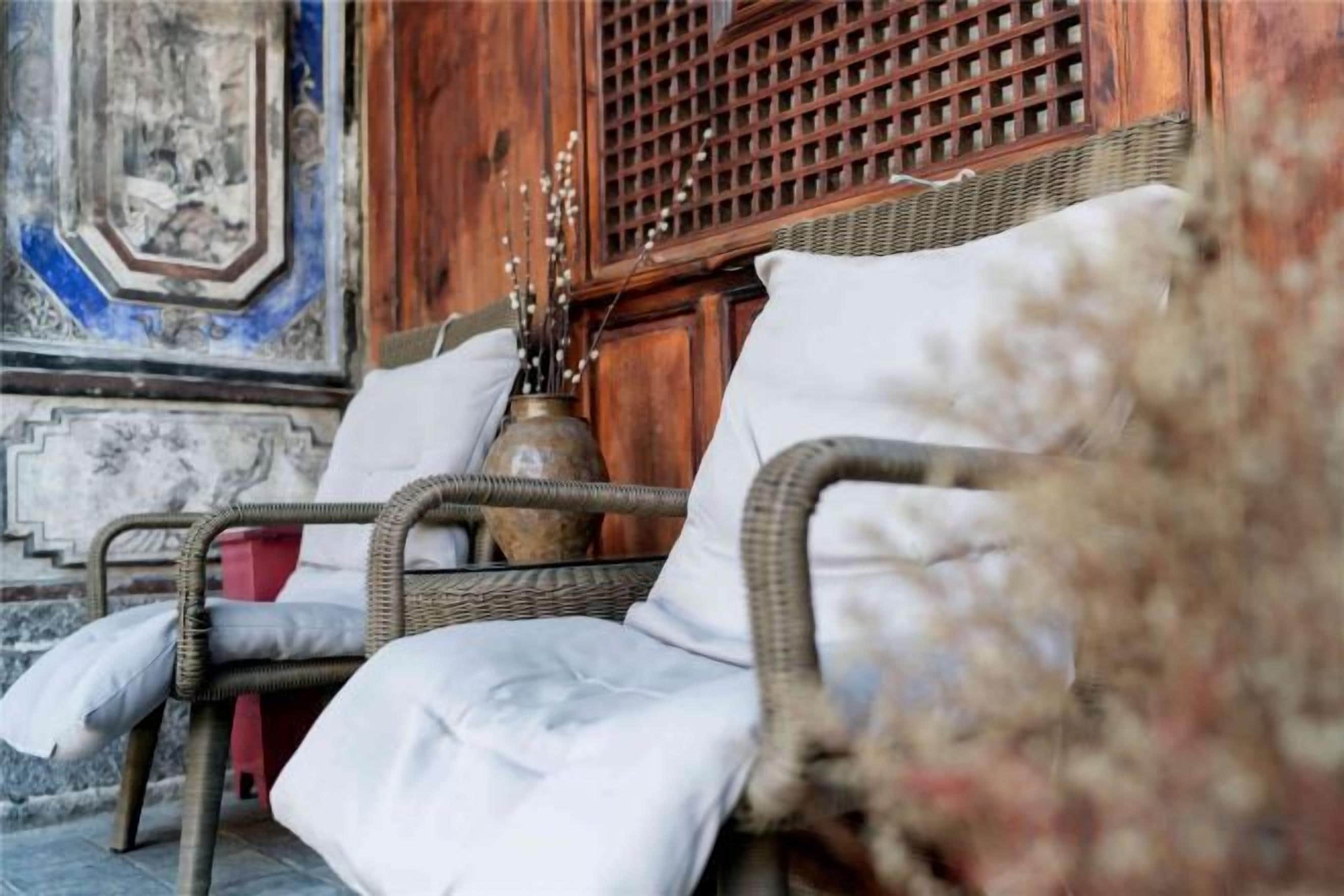 Una silla de mimbre con cojín, un jarrón con ramas y un separador de madera en una habitación con decoración tradicional.