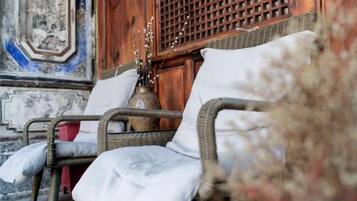 Una silla de mimbre con cojín, un jarrón con ramas y un separador de madera en una habitación con decoración tradicional.