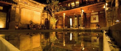 Un patio tradicional con un estanque reflectante, muros de piedra y edificios iluminados.