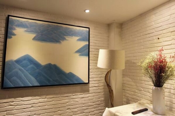 A room with a large framed painting of mountains, a white lamp, and a vase with flowers. - Manyue Wangjiayuan Hostel (Dali City)