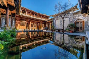 Un patio tradicional con un estanque reflectante, edificios de madera y plantas en macetas.