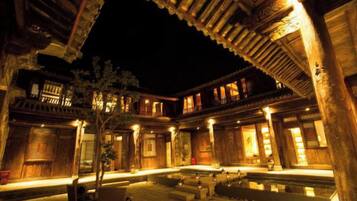 Un patio tradicional con arquitectura de madera, una fuente central e iluminación ambiental.