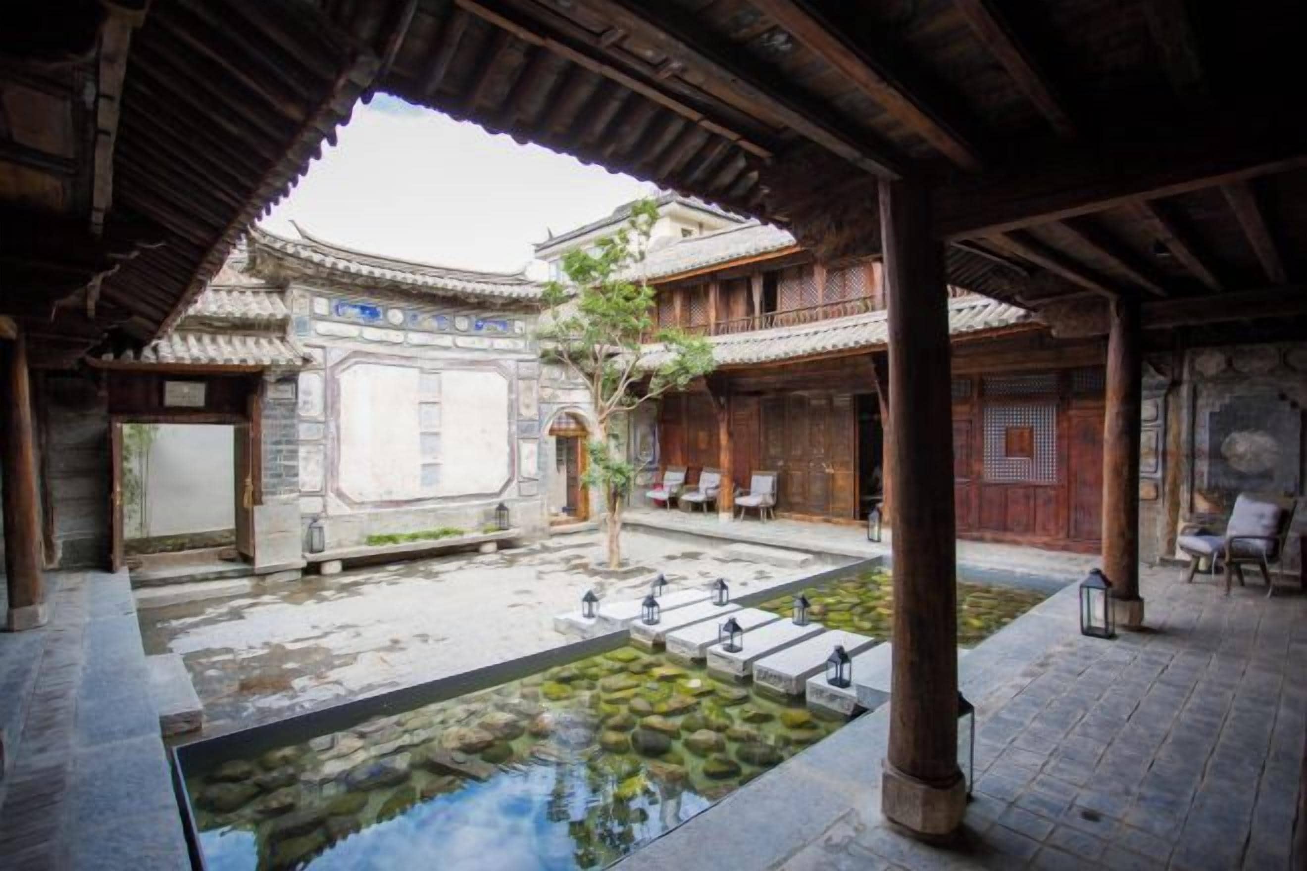 A traditional courtyard with a stone pool, wooden benches, and a tiled roof structure.