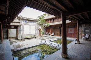Une cour traditionnelle avec une piscine en pierre, des bancs en bois et une structure de toit recouverte de tuiles.