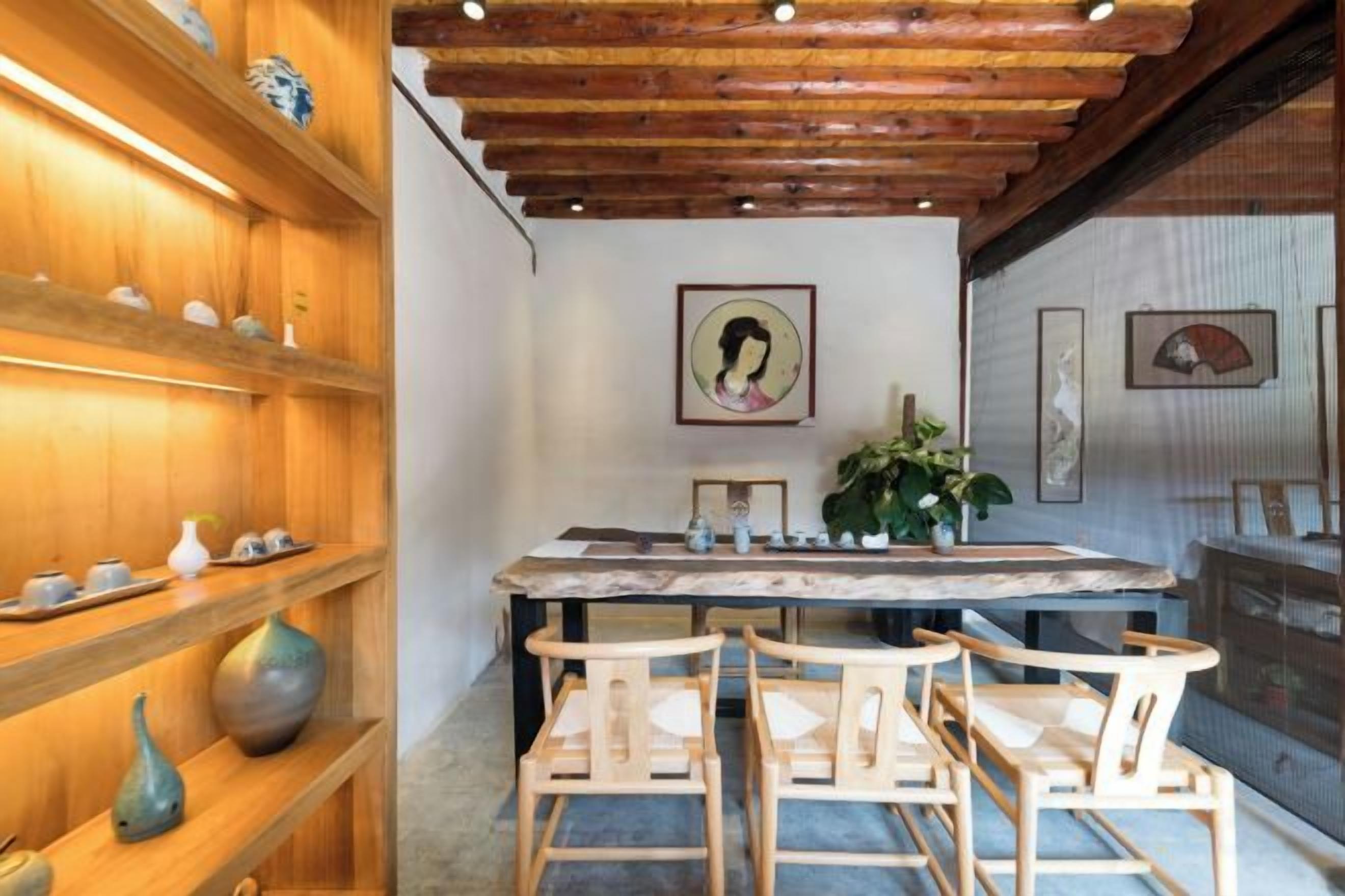 A wooden interior with a dining table and chairs, shelves with decorative items, and framed artwork on the walls.