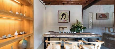 A wooden interior with a dining table and chairs, shelves with decorative items, and framed artwork on the walls.