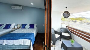 Quarto de hotel com duas camas, varanda com móveis de vime e vista para a rua.