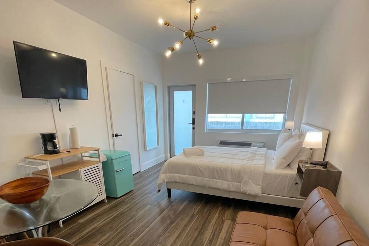 A modern hotel room with a bed, a TV, a desk, and a sofa.