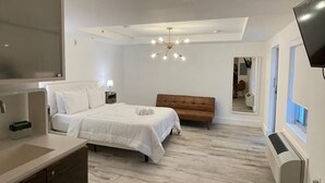 A modern bedroom with a large bed, a wooden bench, a glass table, and a TV mounted on the wall. - Agave on the Beach (Miami Beach)