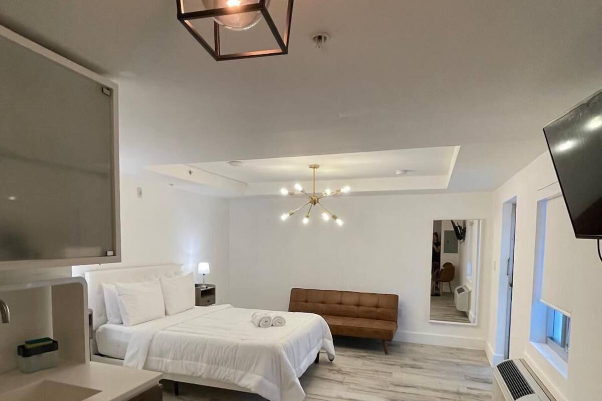 A modern bedroom with a large bed, a wooden bench, a glass table, and a TV mounted on the wall.