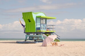 Een bewakingspost met blauw- en groentinten, op een zandstrand met de oceaan op de achtergrond.