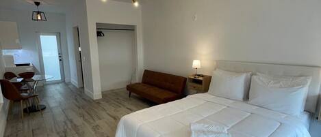 Een moderne slaapkamer met een groot bed, een houten vloer, een bruine bank en een zithoek met een tafel en stoelen.