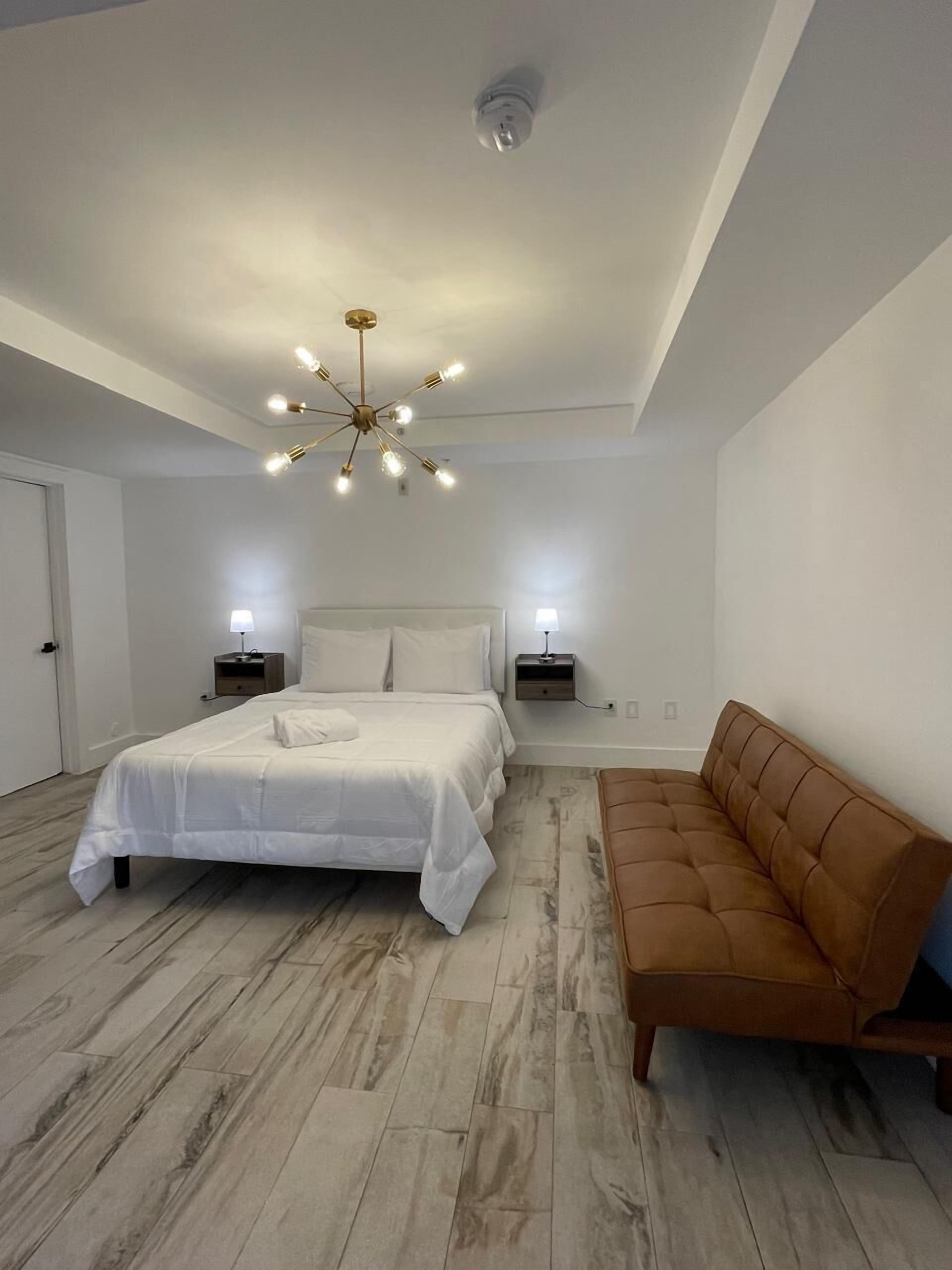 A modern bedroom with a large bed, two bedside tables, a brown sofa, and a unique ceiling light fixture.